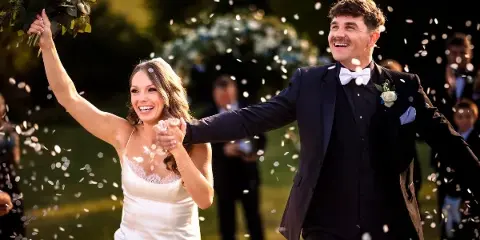 A bride and groom laughing and celebrating with confetti in the air during a wedding.