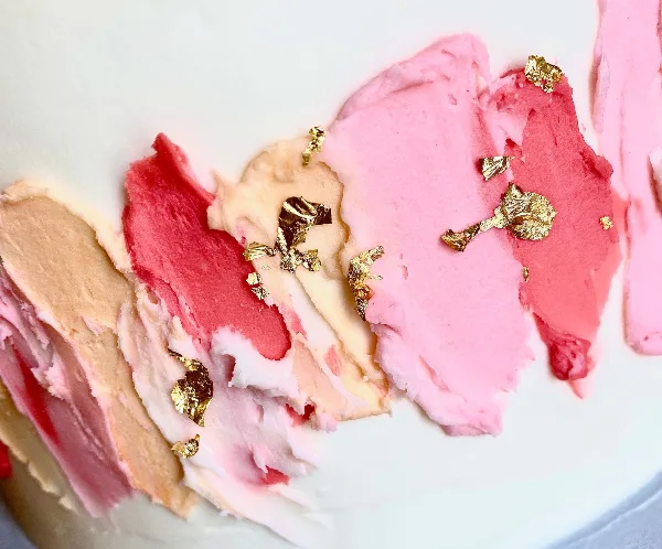 Close-up of a cake decorated with pink and white frosting and gold leaf accents