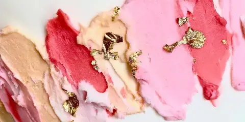Close-up of a cake decorated with pink and white frosting and gold leaf accents