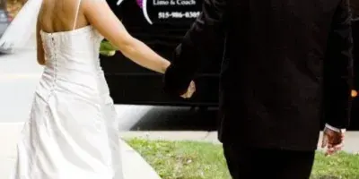A bride and groom walking hand-in-hand toward a black Majestic Limo & Coach Sprinter van.