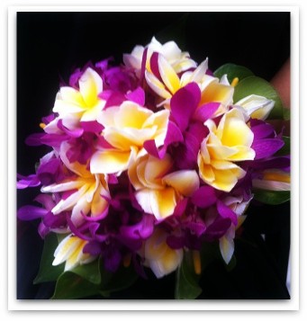 A close-up photograph of a tropical floral arrangement featuring purple and yellow plumeria flowers and orchids.