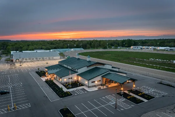 Aerial view of the Warren County Fairgrounds event center building with a large parking lot and surrounding fairgrounds at sunset.