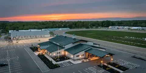 Aerial view of the Warren County Fairgrounds event center building with a large parking lot and surrounding fairgrounds at sunset.