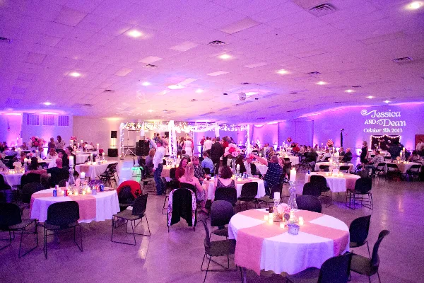 Interior view of a large event hall set up for a wedding reception with round tables and a decorated stage.