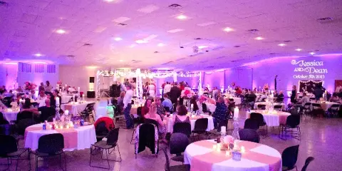 Interior view of a large event hall set up for a wedding reception with round tables and a decorated stage.
