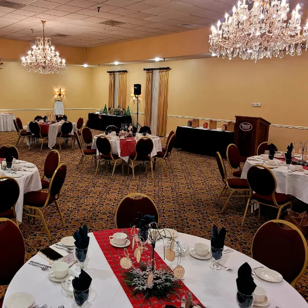 Interior of a banquet hall with round tables set for an event, chandeliers, and a podium labeled Spartan Manor.