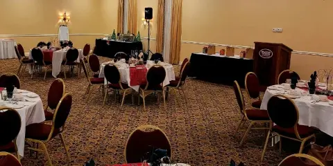 Interior of a banquet hall with round tables set for an event, chandeliers, and a podium labeled Spartan Manor.