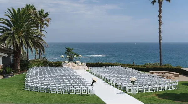 Rows of white chairs arranged for an outdoor wedding ceremony on a lawn overlooking the ocean.