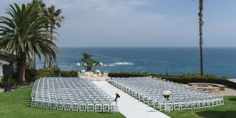 Rows of white chairs arranged for an outdoor wedding ceremony on a lawn overlooking the ocean.
