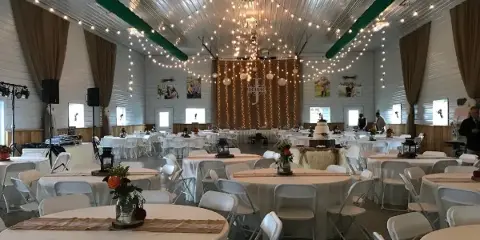 Interior of a rustic barn venue set up for a wedding with round tables, white chairs, and string lights.