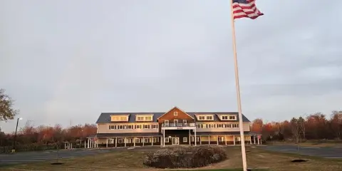 Exterior view of a two-story commercial building with a flagpole and a rainbow in the sky.
