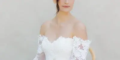 A bride in a white lace gown with a sleek updo and soft makeup, holding a bouquet of yellow roses.