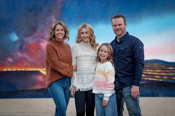 A family of four posing for a professional portrait in front of a colorful studio backdrop.
