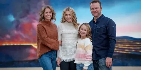 A family of four posing for a professional portrait in front of a colorful studio backdrop.