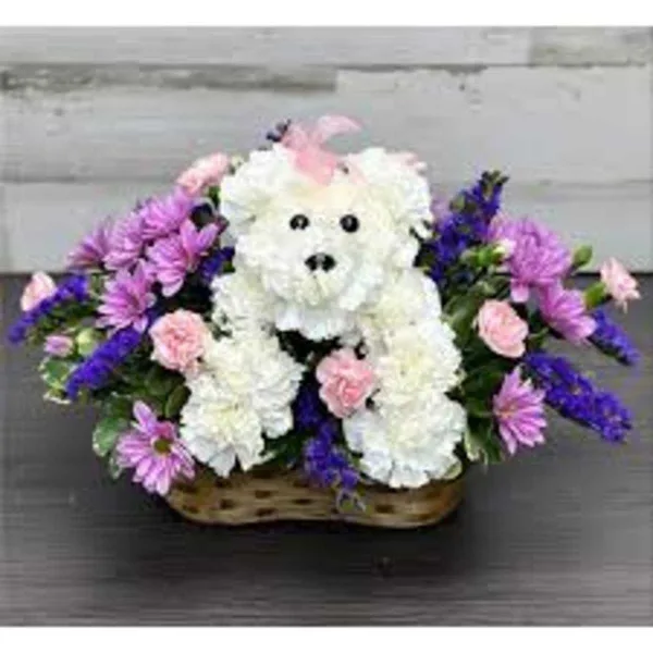 A white floral teddy bear arrangement in a basket surrounded by pink and purple flowers