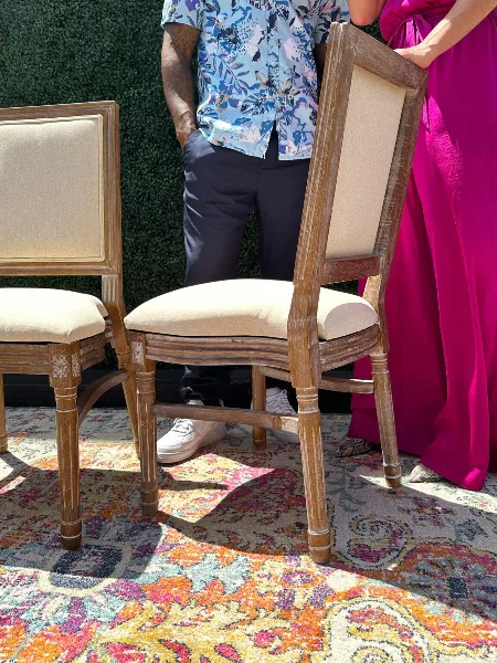 Two upholstered wooden chairs and a patterned rug displayed outdoors, representing event furniture rentals.