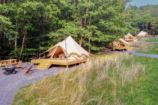 Wide shot of a glamping resort featuring canvas bell tents on wooden decks surrounded by a forest and gravel pathways.