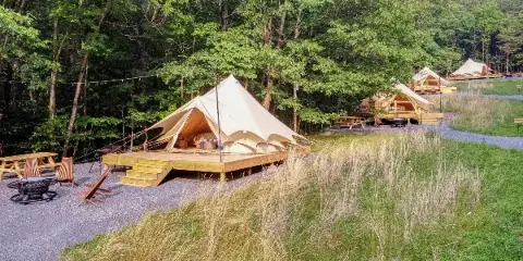 Wide shot of a glamping resort featuring canvas bell tents on wooden decks surrounded by a forest and gravel pathways.