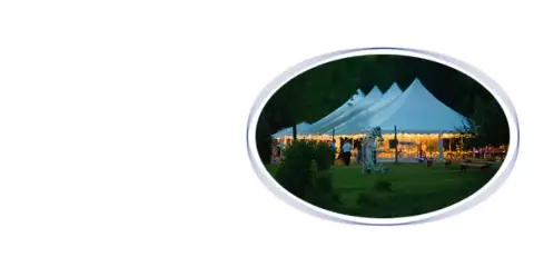 A large white event tent set up on a grassy lawn at dusk.