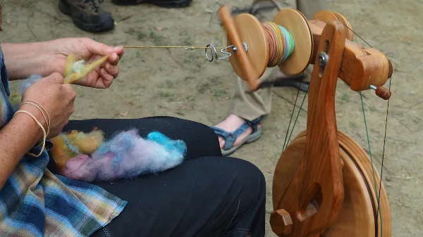 A person spinning colorful wool fiber on a wooden spinning wheel during a workshop.