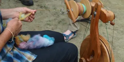 A person spinning colorful wool fiber on a wooden spinning wheel during a workshop.
