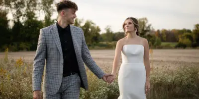 A bride and groom holding hands and walking in a field during a wedding photoshoot.
