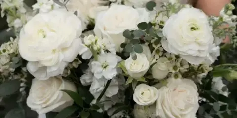 A bride in a white lace dress holding a large bouquet of white roses, ranunculus, and eucalyptus.