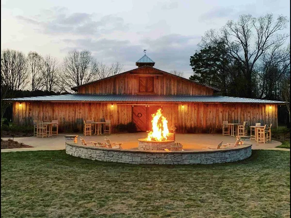 Exterior view of a wooden barn wedding venue with a fire pit and outdoor seating at dusk.