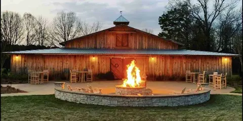 Exterior view of a wooden barn wedding venue with a fire pit and outdoor seating at dusk.