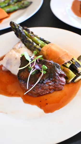 A plated meal consisting of a seared steak, roasted asparagus, and a side of mashed potatoes served with a red wine reduction sauce.