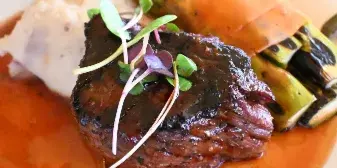 A plated meal consisting of a seared steak, roasted asparagus, and a side of mashed potatoes served with a red wine reduction sauce.