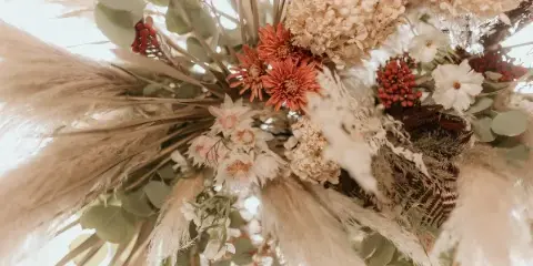A close-up of a wedding floral arrangement featuring pampas grass, dried hydrangeas, and orange and white flowers.