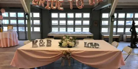 Interior of a wedding venue with a table decorated with 'Bride to Be' balloons and 'K&B Love' signs.