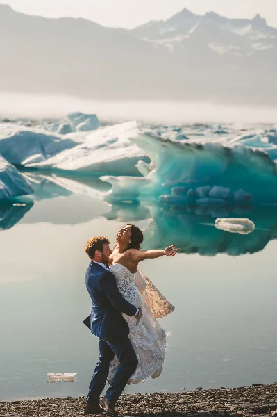 A bride and groom dancing in front of a turquoise glacier and mountain range.
