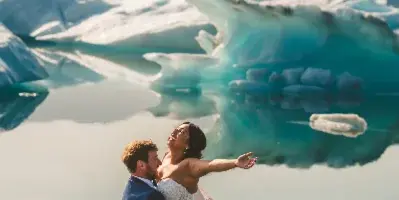 A bride and groom dancing in front of a turquoise glacier and mountain range.