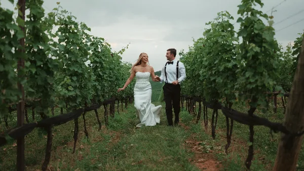 A bride and groom walking hand-in-hand through a vineyard row, captured in a cinematic style.