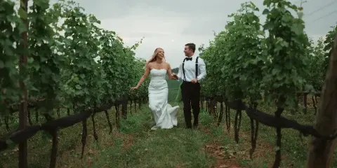 A bride and groom walking hand-in-hand through a vineyard row, captured in a cinematic style.