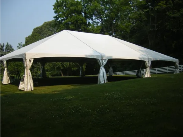 A large white frame tent with tied-back side walls set up on a grassy lawn.