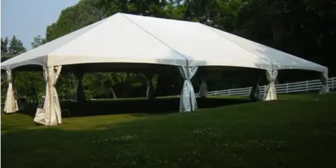 A large white frame tent with tied-back side walls set up on a grassy lawn.