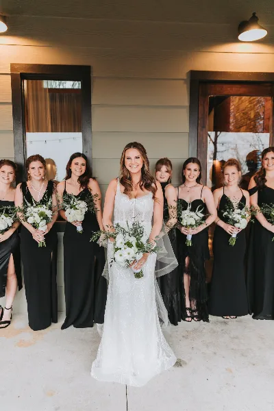A bride in a white gown standing with her bridesmaids in black dresses, all holding white bouquets.