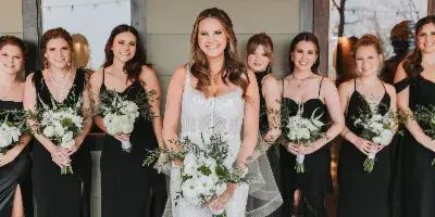 A bride in a white gown standing with her bridesmaids in black dresses, all holding white bouquets.
