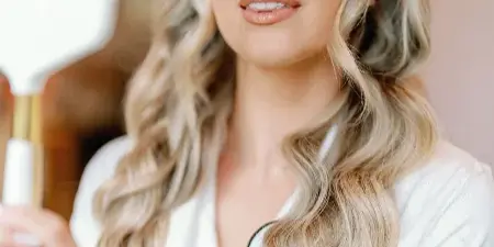 A bride with styled blonde hair and makeup looking into a hand mirror.