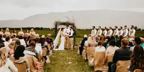 Outdoor wedding ceremony at a rustic venue with a wooden arch and mountain views