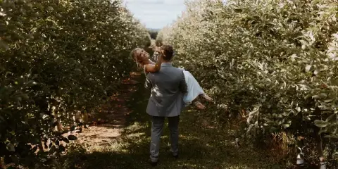 A bride and groom dancing in the aisle of an apple orchard.