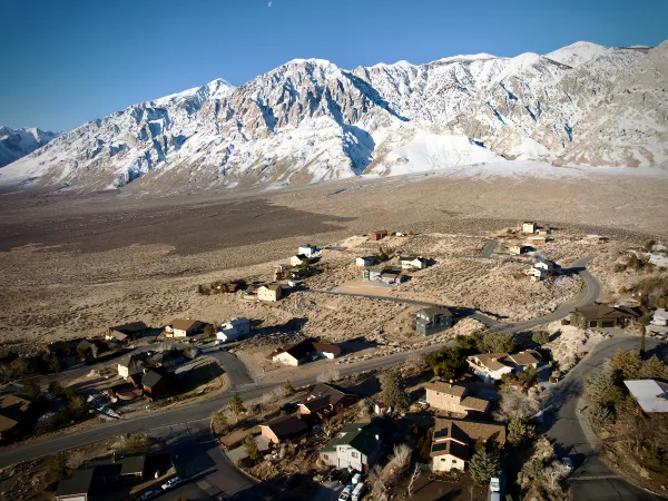 Aerial view of a small town with houses and roads set against a backdrop of snow-capped mountains.