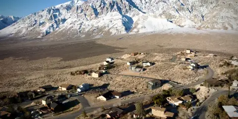 Aerial view of a small town with houses and roads set against a backdrop of snow-capped mountains.