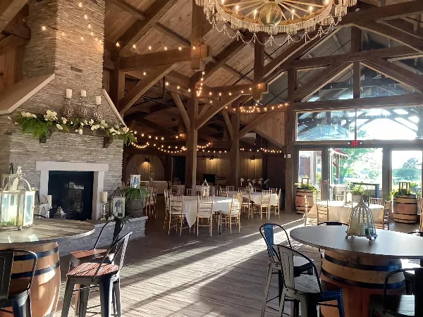 Interior view of a rustic event venue with a stone fireplace, wooden beams, and tables set for a gathering.