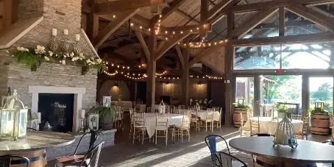 Interior view of a rustic event venue with a stone fireplace, wooden beams, and tables set for a gathering.