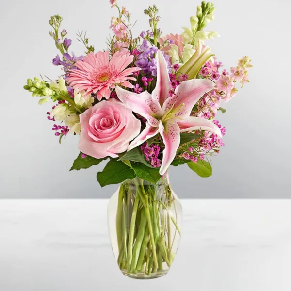 A floral arrangement with a pink rose, a pink lily, and a pink gerbera daisy in a clear glass vase.