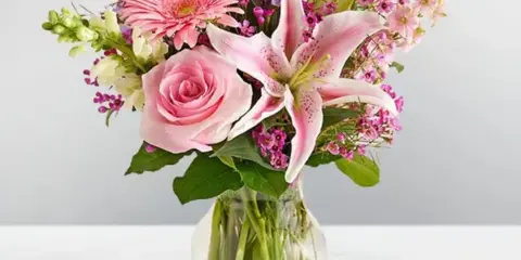 A floral arrangement with a pink rose, a pink lily, and a pink gerbera daisy in a clear glass vase.
